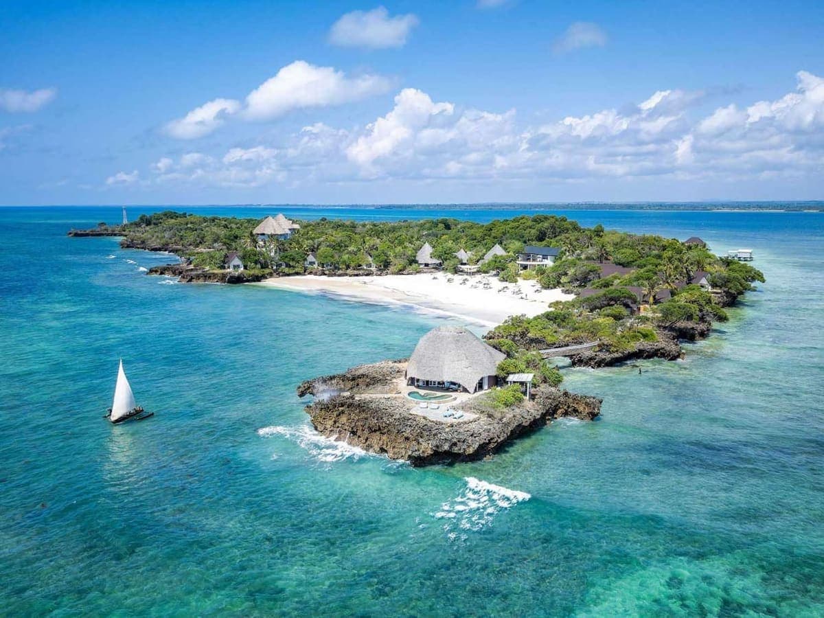 Aerial view of Chale Island ringed by white sand and reef, with a dhow sailing past