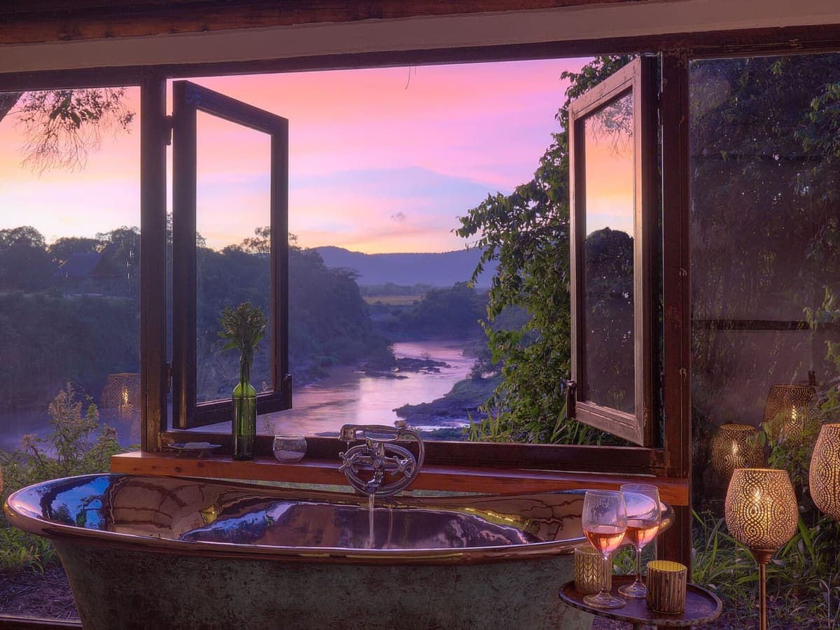 A copper bathtub beside open windows looking over the river at sunset at House in the Wild
