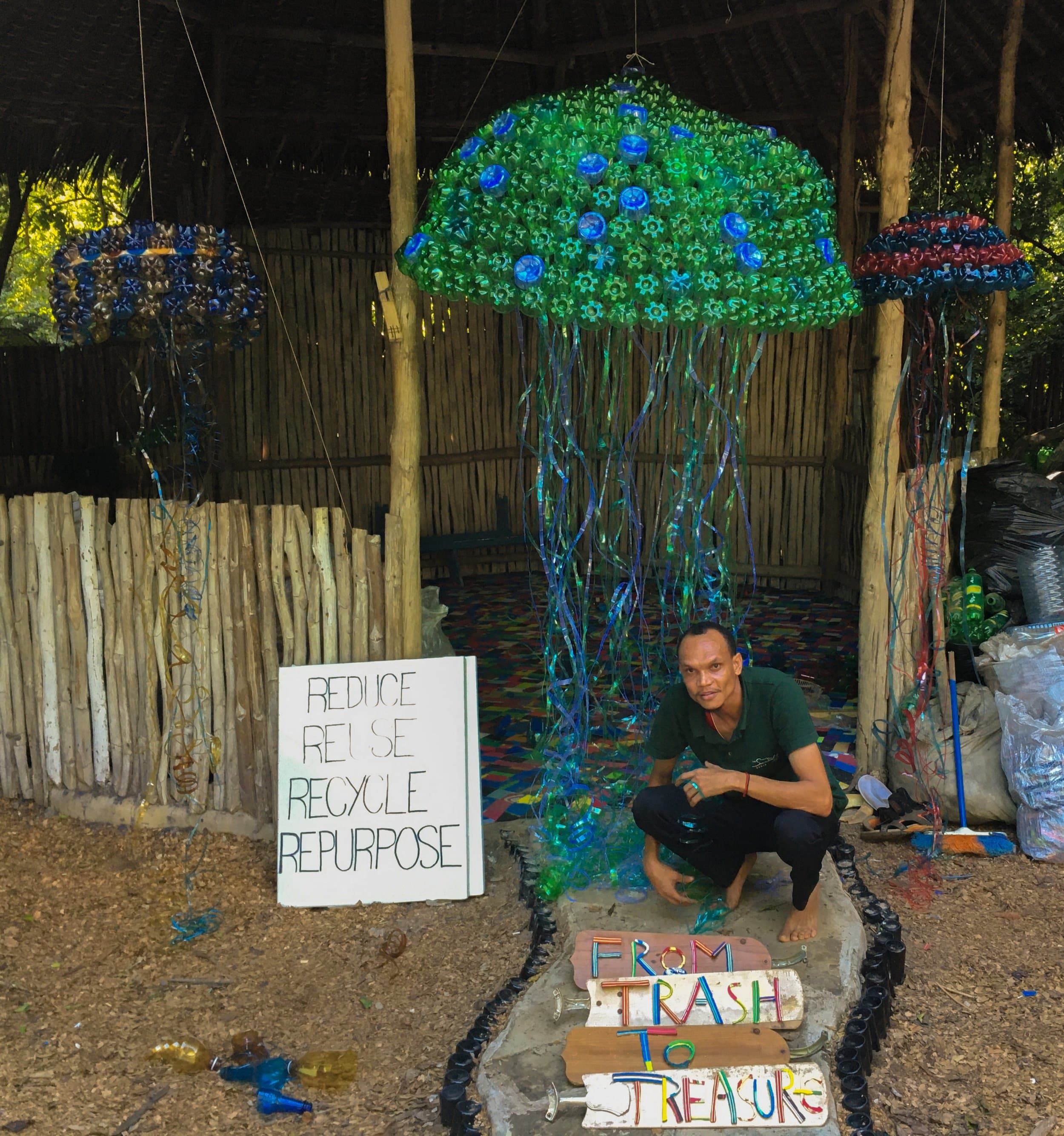 Jellyfish sculptures made from recycled plastic bottles hang above signs reading 'Reduce, Reuse, Recycle, Repurpose' and 'From Trash to Treasure'