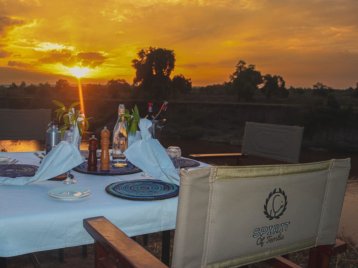 A dinner table set on the Mara riverbank at sunset at Tembo by Jackson Collection
